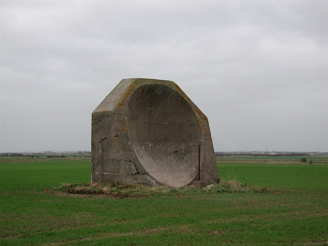 A large disc-shaped concrete acoustic mirror standing in a field at Kilnsea, England